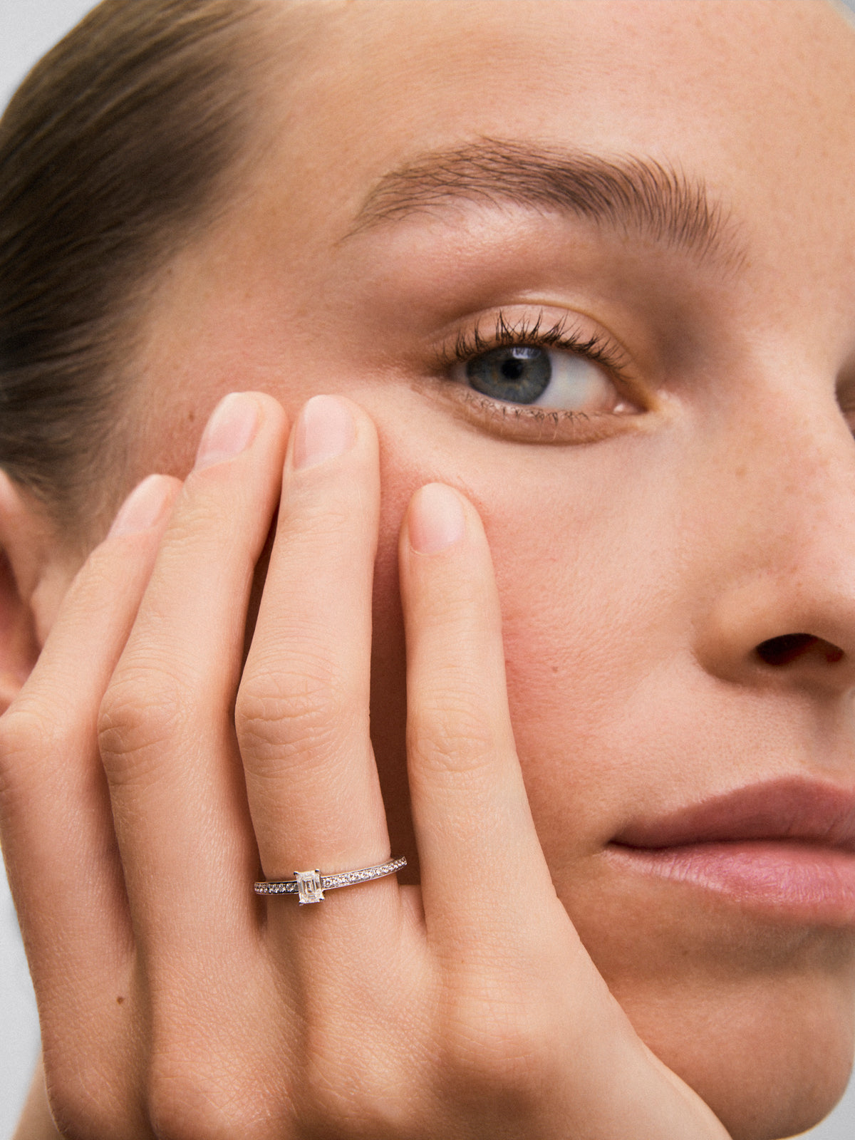 Anillo de oro blanco de 18K con diamante central en talla esmeralda de 0,25 y brazo de 16 diamantes en talla brillante