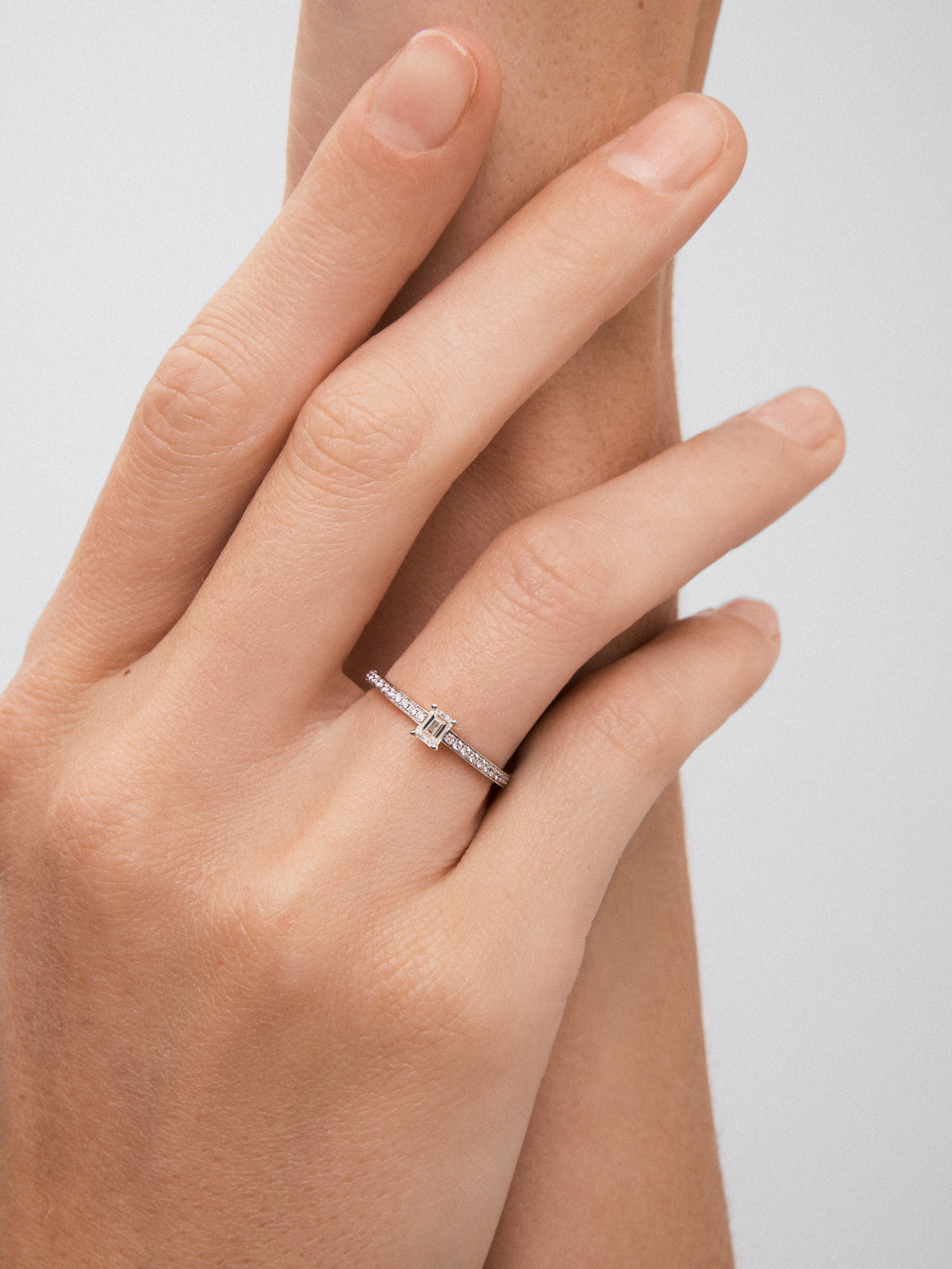 Anillo de oro blanco de 18K con diamante central en talla esmeralda de 0,25 y brazo de 16 diamantes en talla brillante