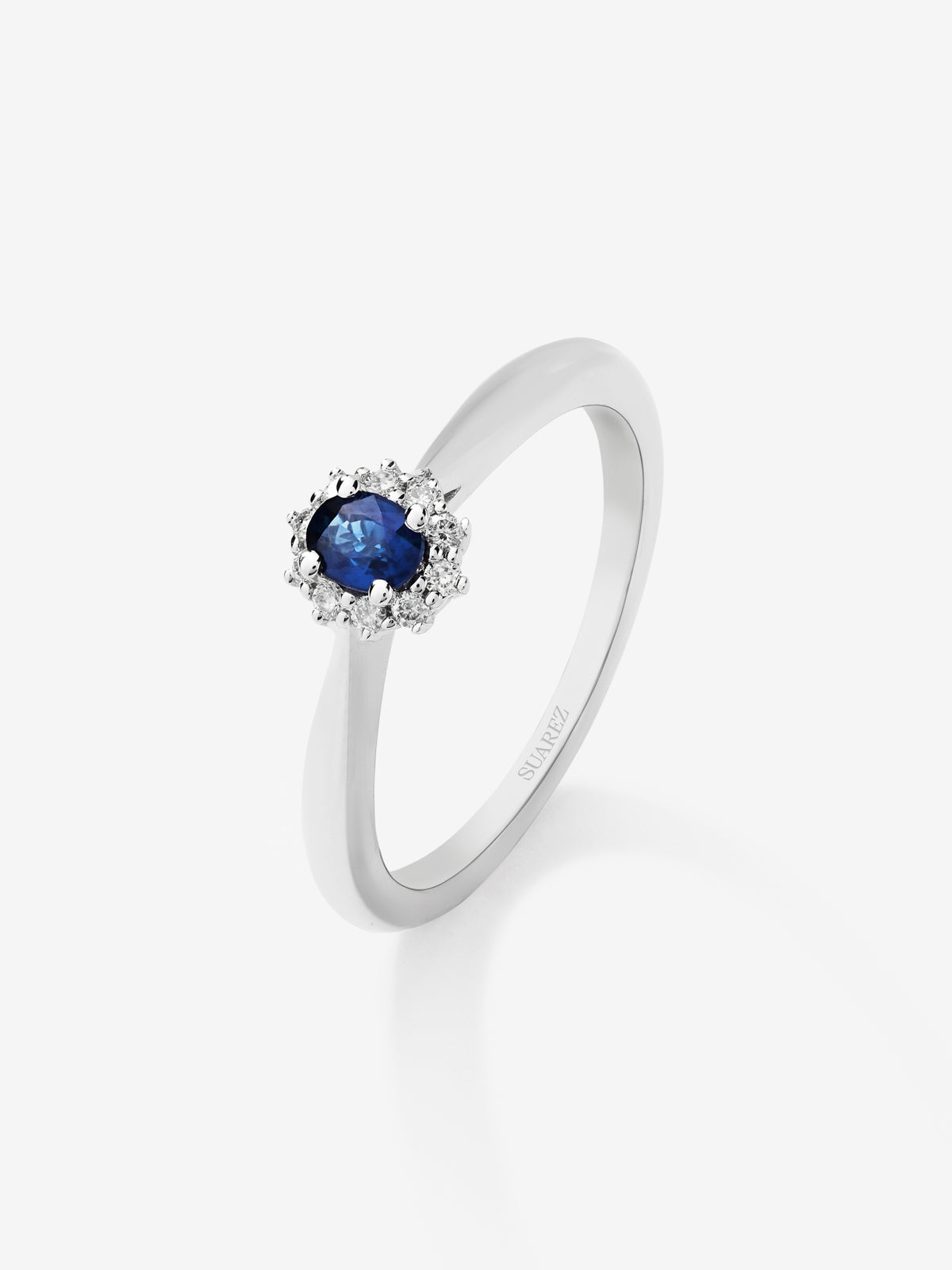 Anillo de oro blanco de 18K con zafiro azul central en talla oval de 0,20 cts y orla de diamantes en talla brillante
