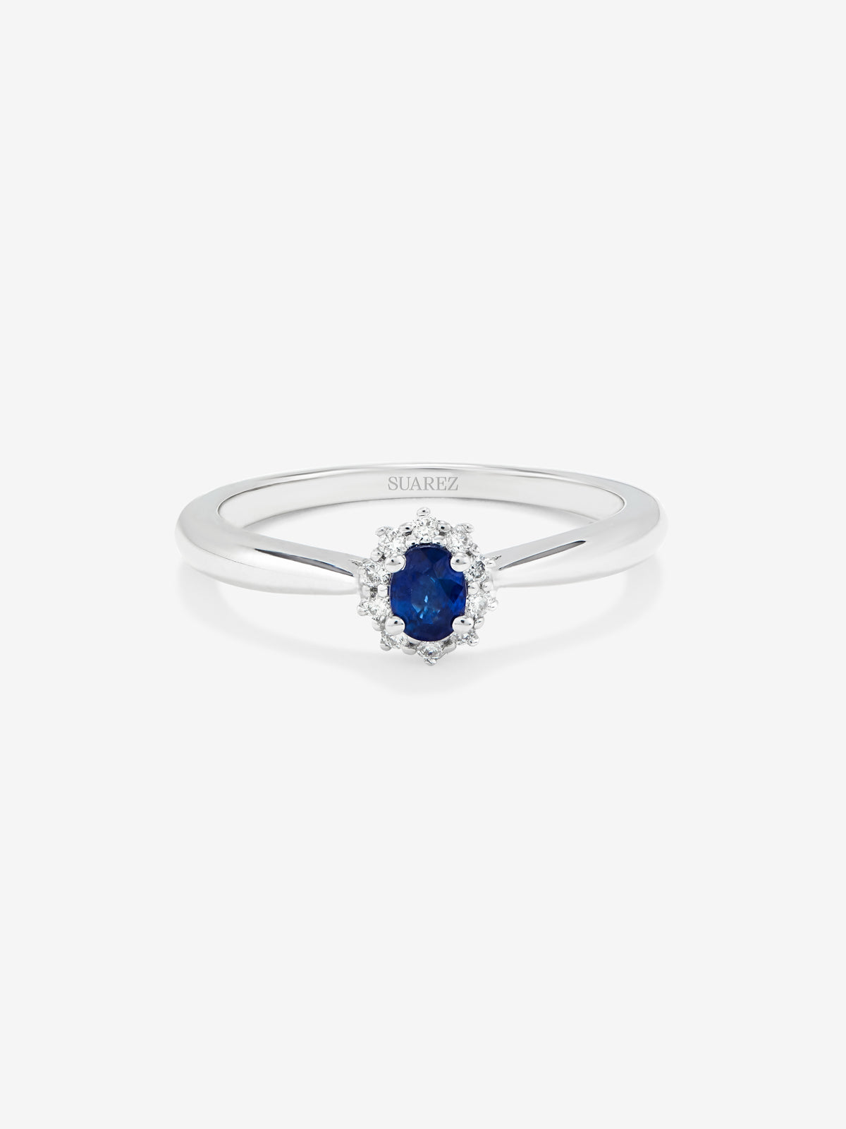 Anillo de oro blanco de 18K con zafiro azul central en talla oval de 0,20 cts y orla de diamantes en talla brillante