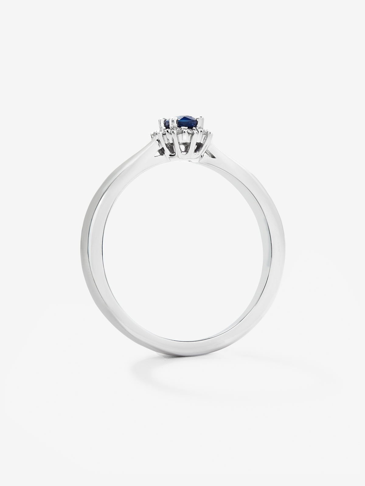Anillo de oro blanco de 18K con zafiro azul central en talla oval de 0,20 cts y orla de diamantes en talla brillante