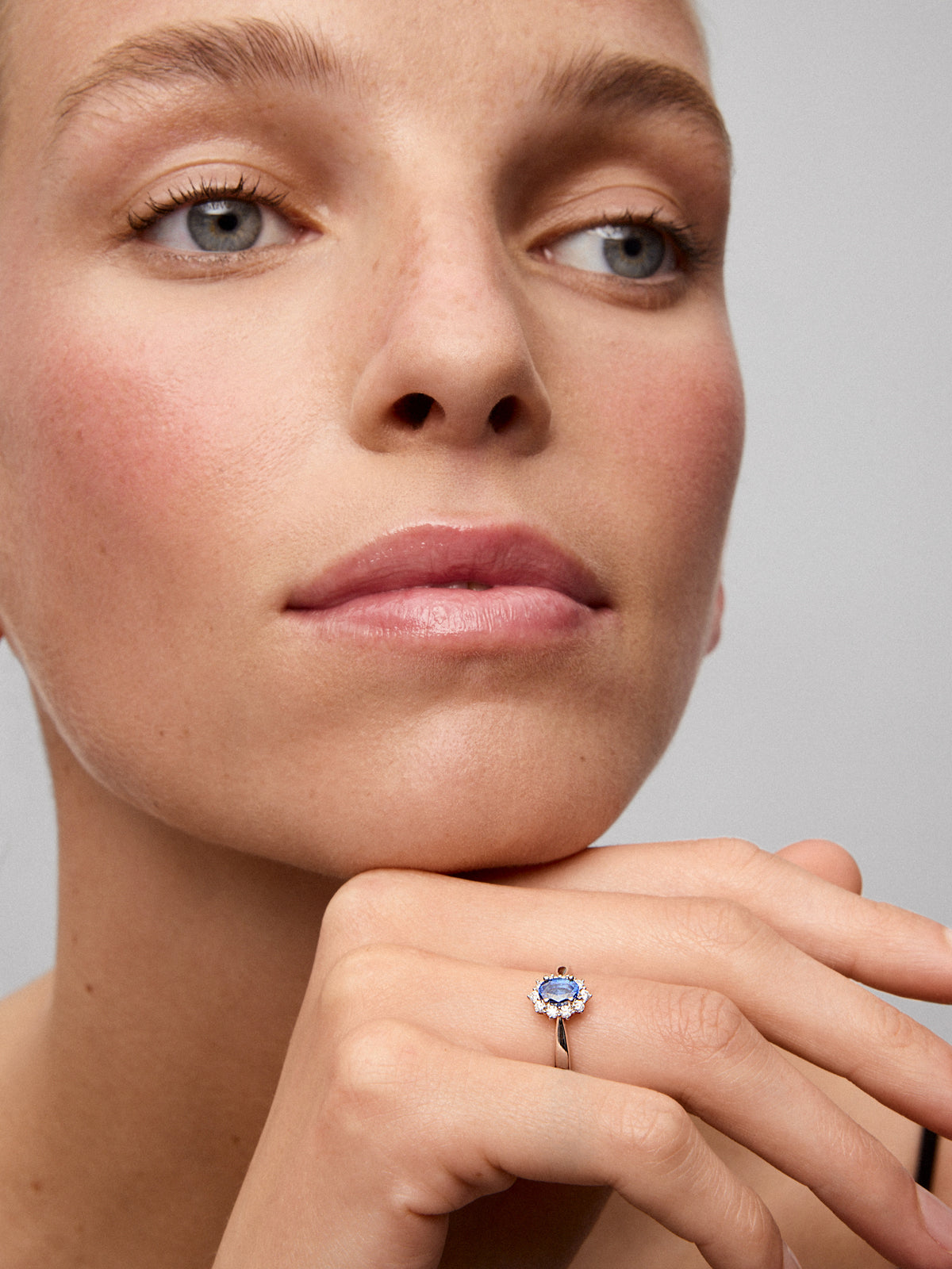 Anillo de oro blanco de 18K con zafiro azul central en talla oval de 0,60 cts y orla de diamantes en talla brillante