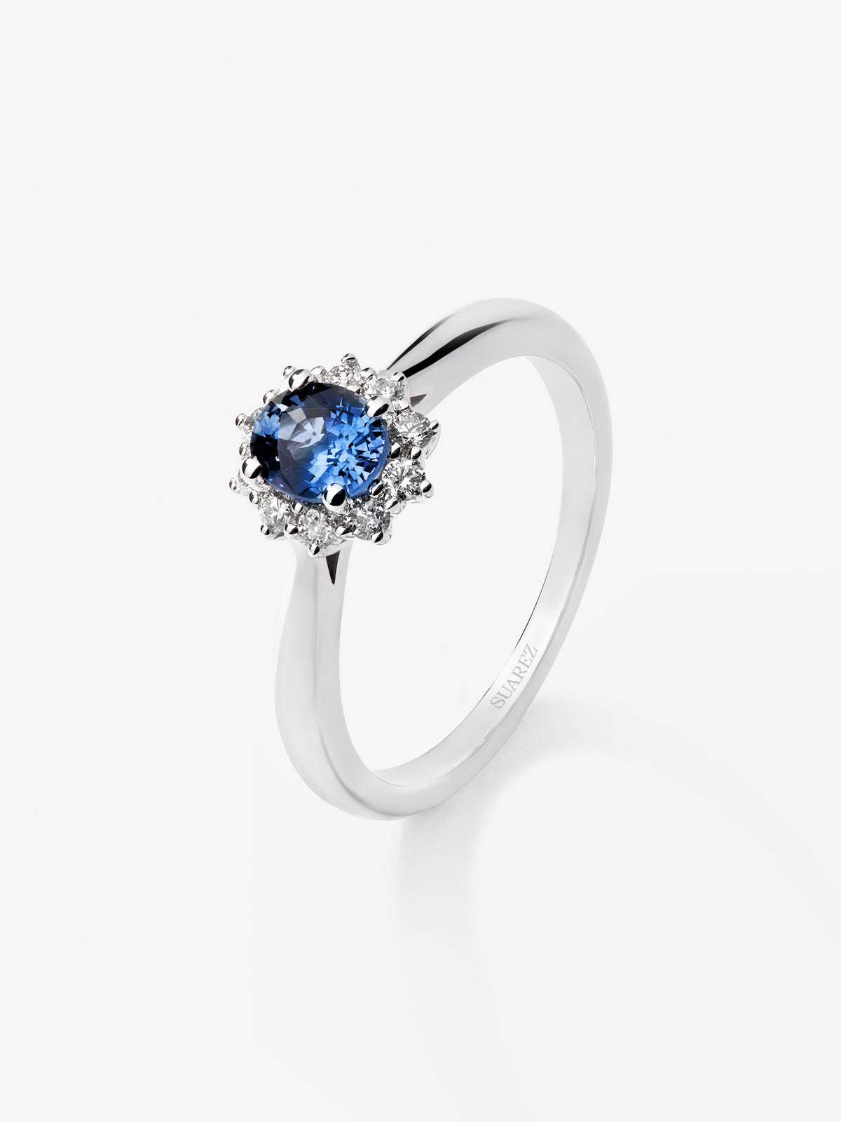 Anillo de oro blanco de 18K con zafiro azul central en talla oval de 0,30 cts y orla de diamantes en talla brillante