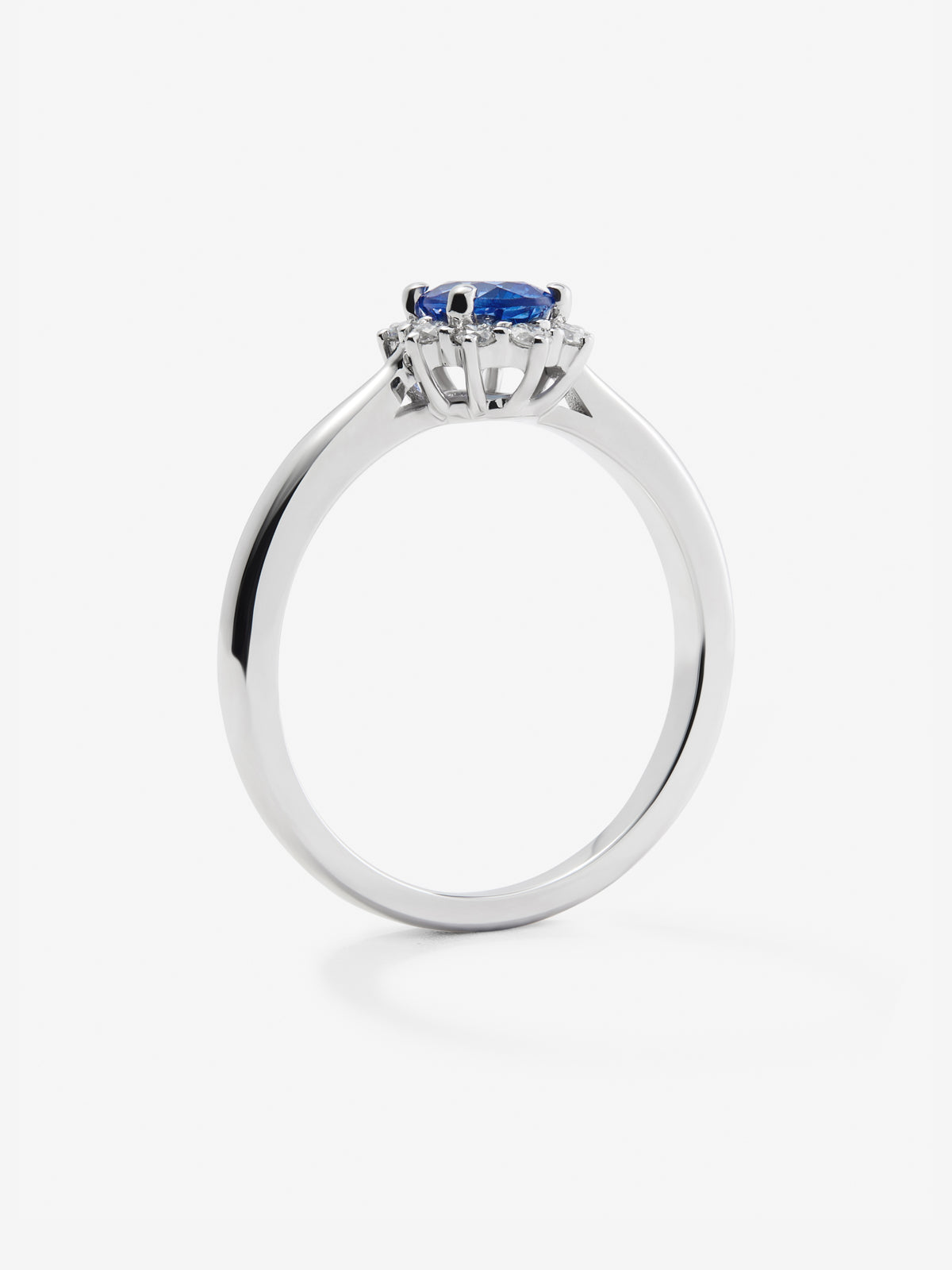Anillo de oro blanco de 18K con zafiro azul central en talla oval de 0,30 cts y orla de diamantes en talla brillante