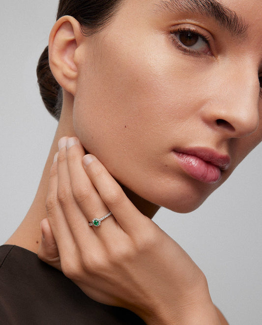 Anillo de oro blanco de 18K con esmeralda en talla brillante de 0,15 cts y brazo y orla de 26 diamantes en talla brillante con un total de 0,27 cts