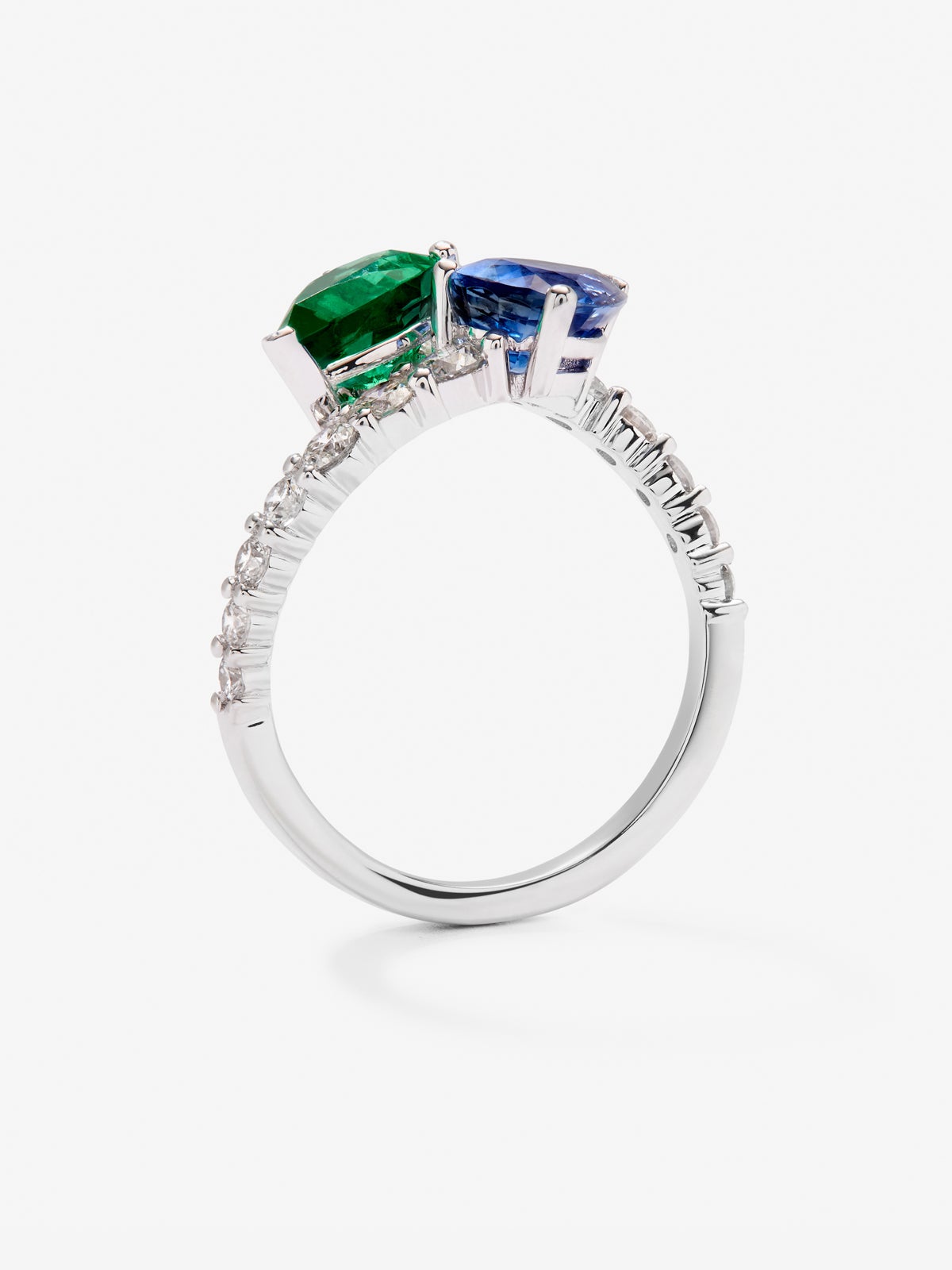 Anillo tú y yo de oro blanco de 18K con un zafiro azul intenso en talla pera de 1,49 cts, una esmeralda verde en talla pera de 1,04 cts y 14 diamantes en talla brillante con un total de 0,64 cts