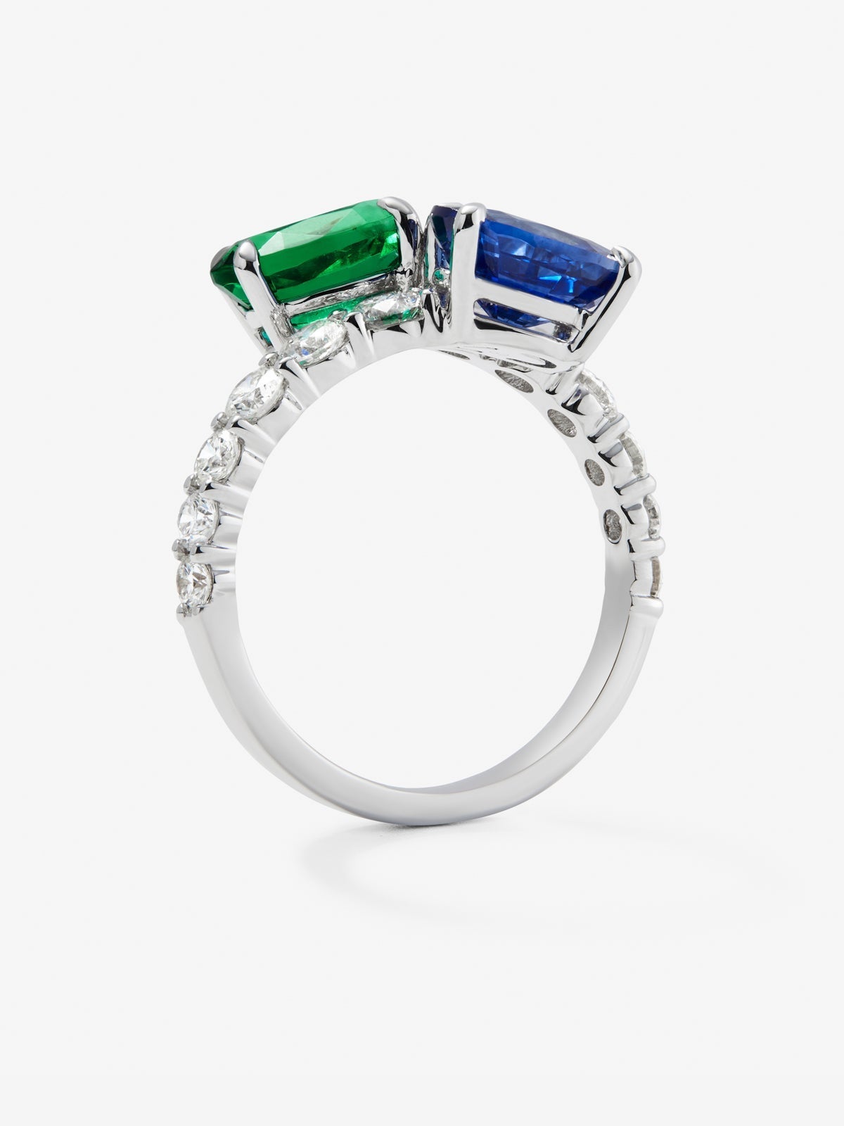 Anillo tú y yo de oro blanco de 18K con zafiro azul en talla oval de 1,75 cts, esmeralda en talla oval de 1,28 cts y 12 diamantes en talla brillante con un total de 0,25 cts
