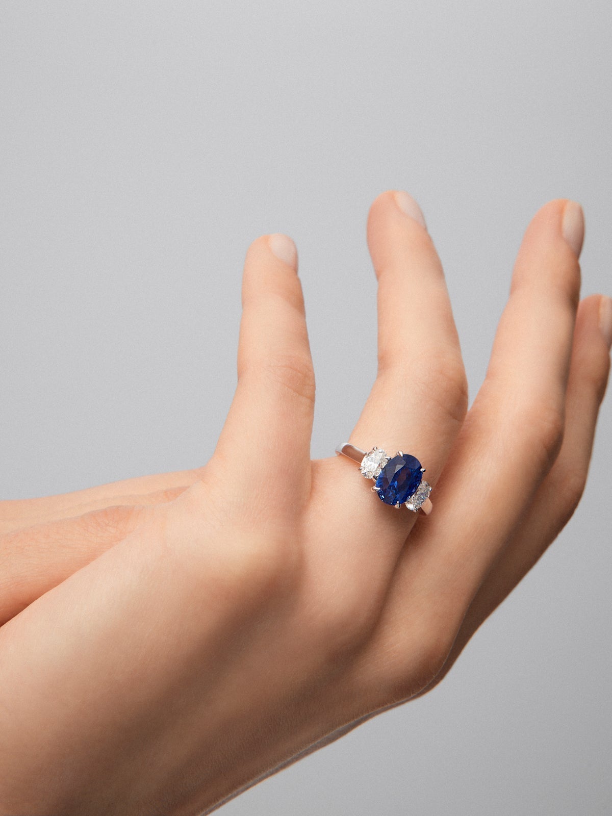 Anillo tresillo de oro blanco de 18K con zafiro azul royal en talla oval de 3,37 cts y 2 diamantes en talla oval con un total de 0,8 cts