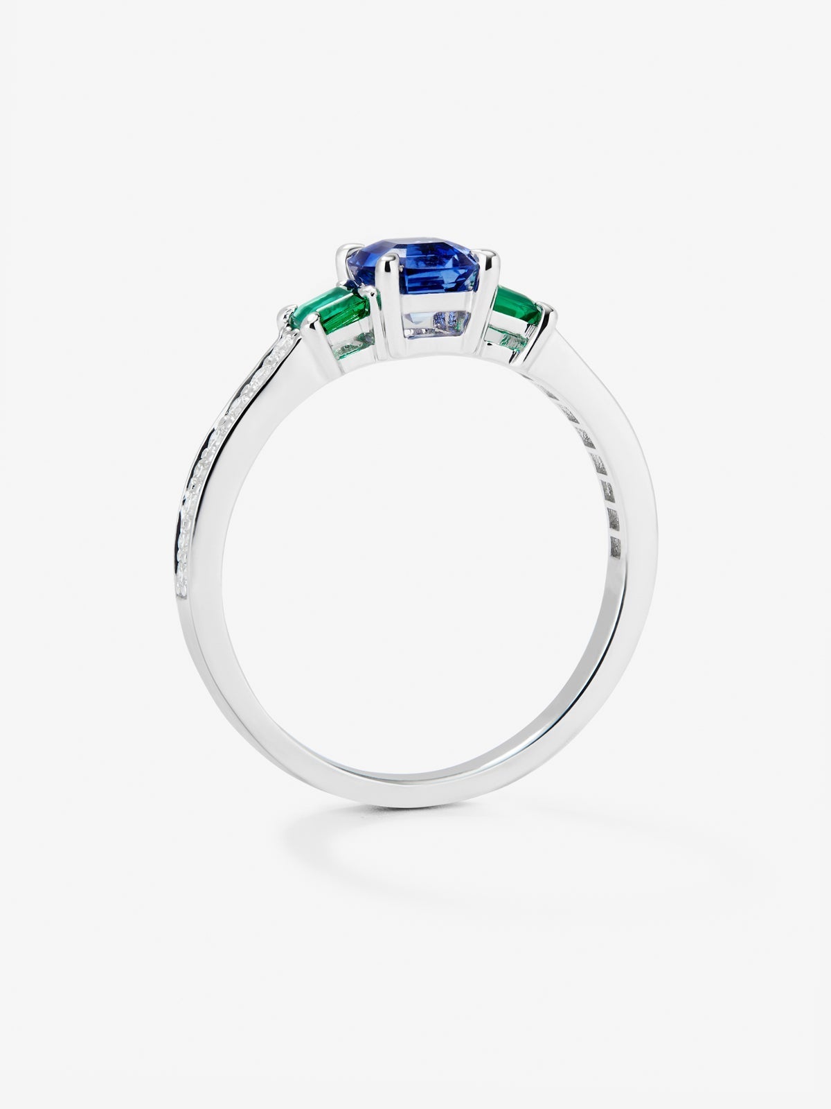 Anillo tresillo de oro blanco de 18K con zafiro azul en talla esmeralda de 0,71 cts, esmeraldas verdes en talla octogonal de 0,21 cts y diamantes blancos en talla brillante de 0,02 cts