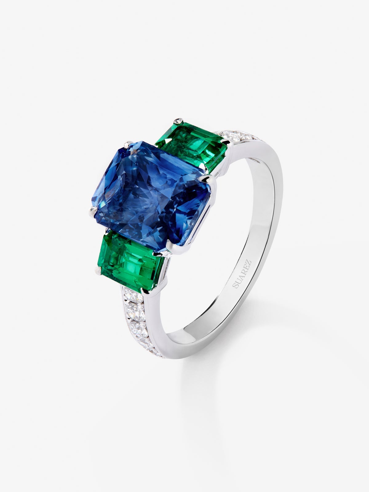 Anillo tresillo de oro blanco de 18K con zafiro azul en talla esmeralda de 3,6 cts, esmeraldas verdes en talla octogonal de 1,12 cts y diamantes blancos en talla brillante de 0,073 cts
