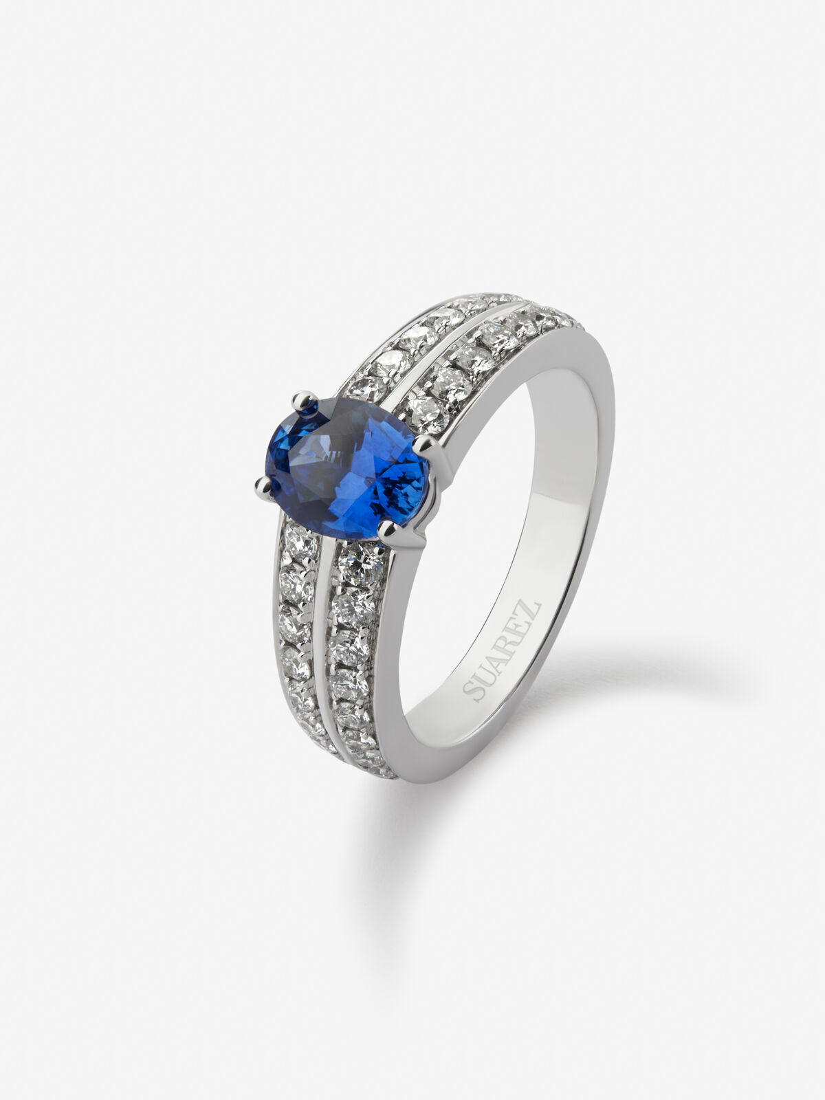 Anillo de oro blanco de 18K con zafiro azul vivid en talla oval de 1 292 cts y 32 diamantes en talla brillante con un total de 0 6 cts Suarez
